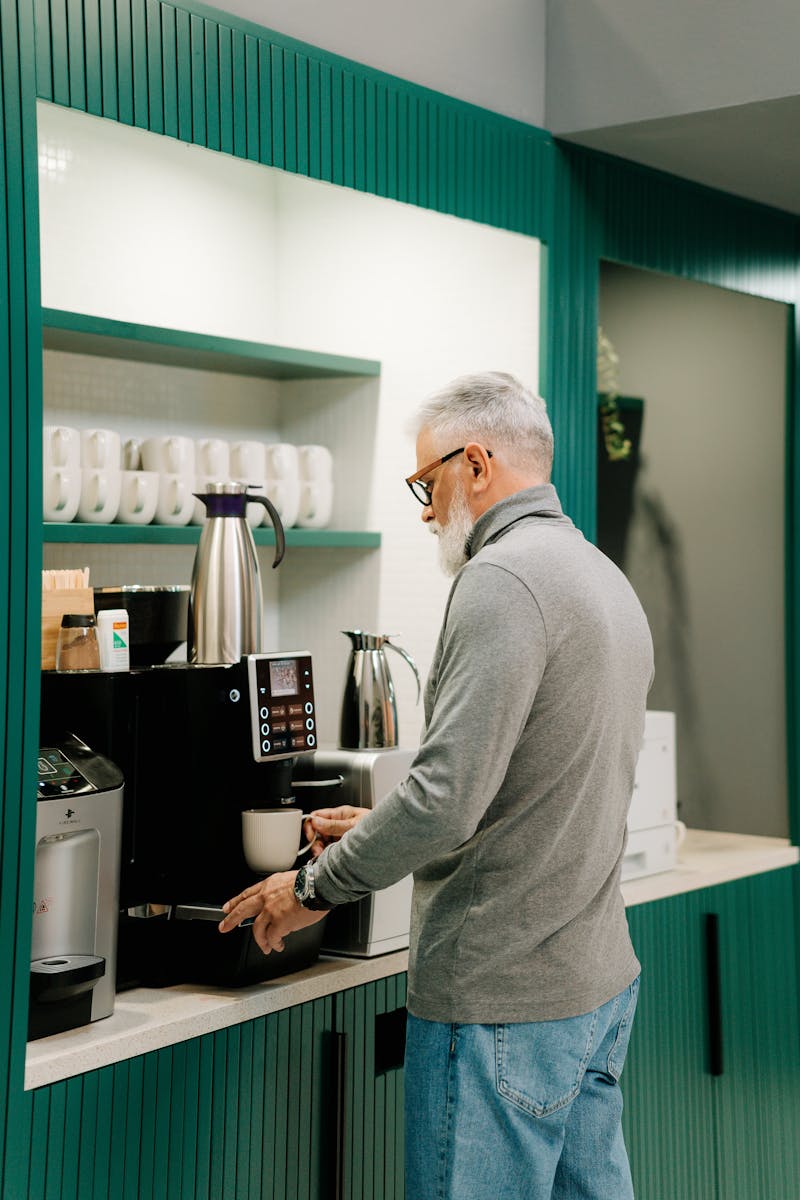 A senior man prepares coffee using a machine in a contemporary office setting.