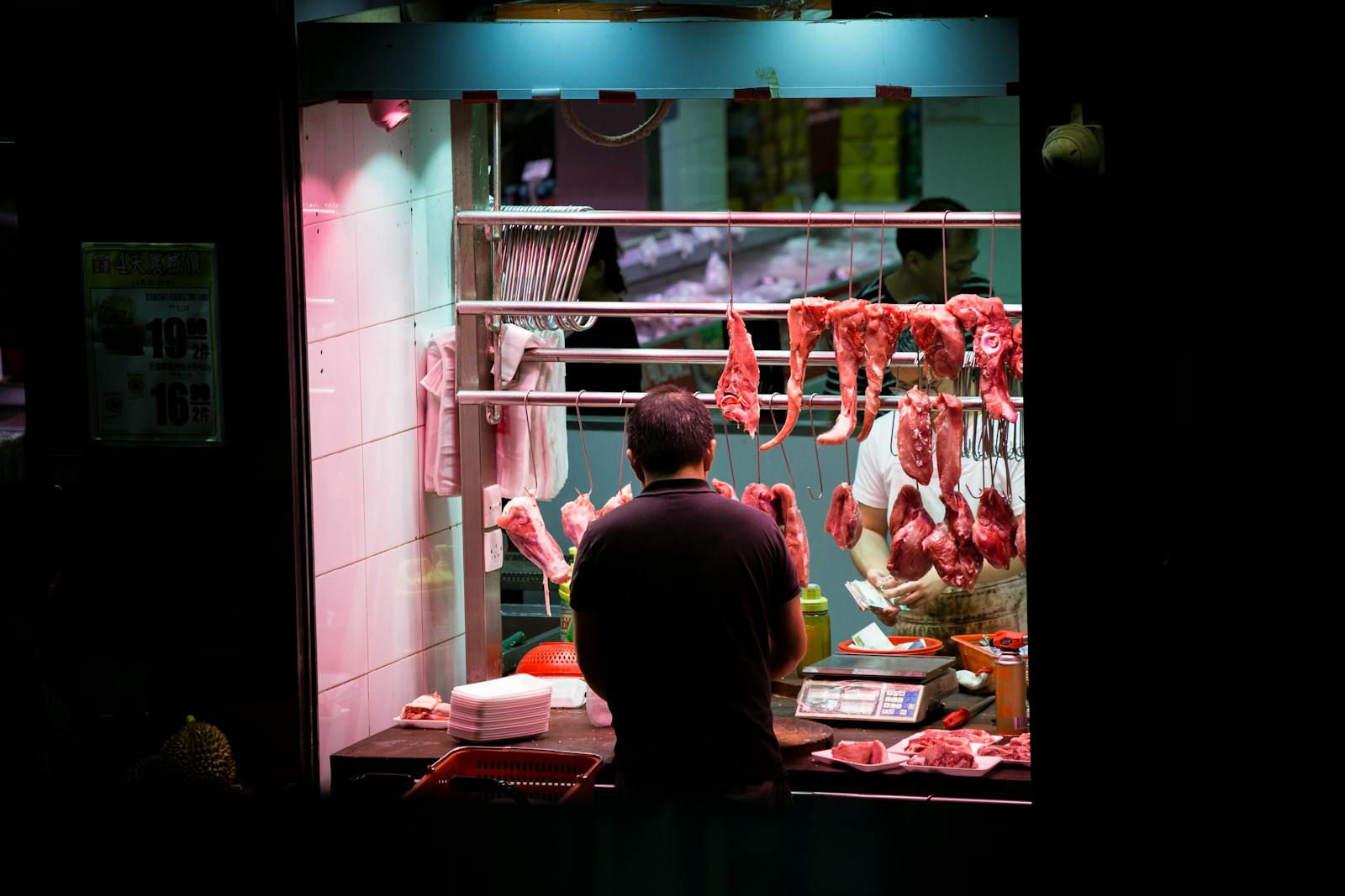 Butcher working in a vibrant Hong Kong market stall preparing fresh cuts of meat.